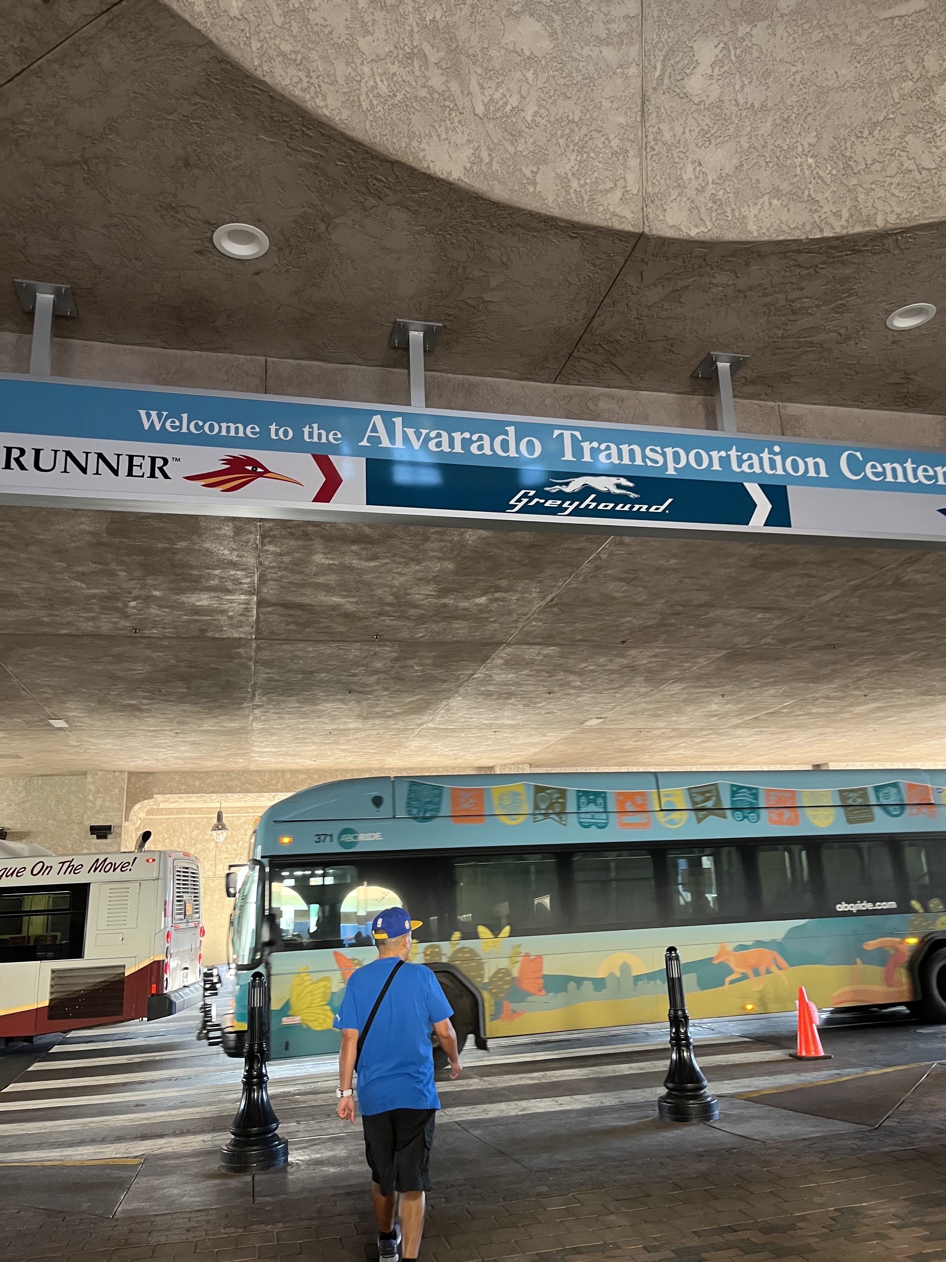 A man walking while a bus passes by in the Alvarado Transportation Center.